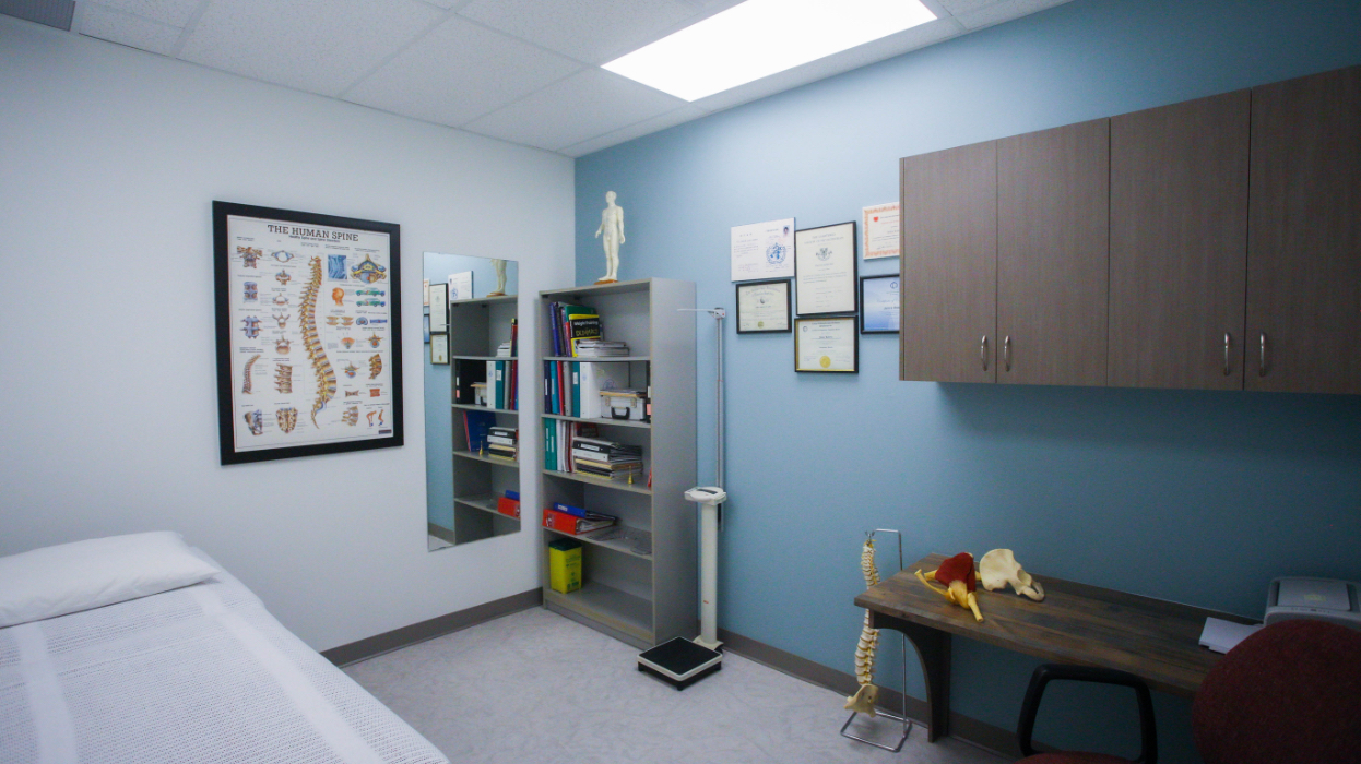 Physiotherapy room with bed, desk, book shelf and demonstration models.