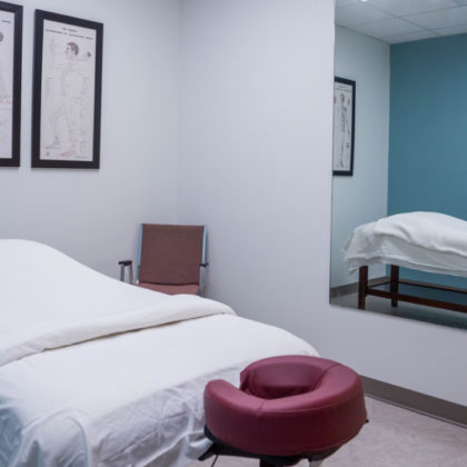 Massage room One at our Wynford location featuring a bed, mirror and artwork on the walls
